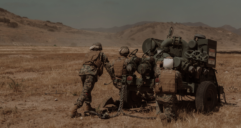 Marines in combat gear moving field equipment across a training range