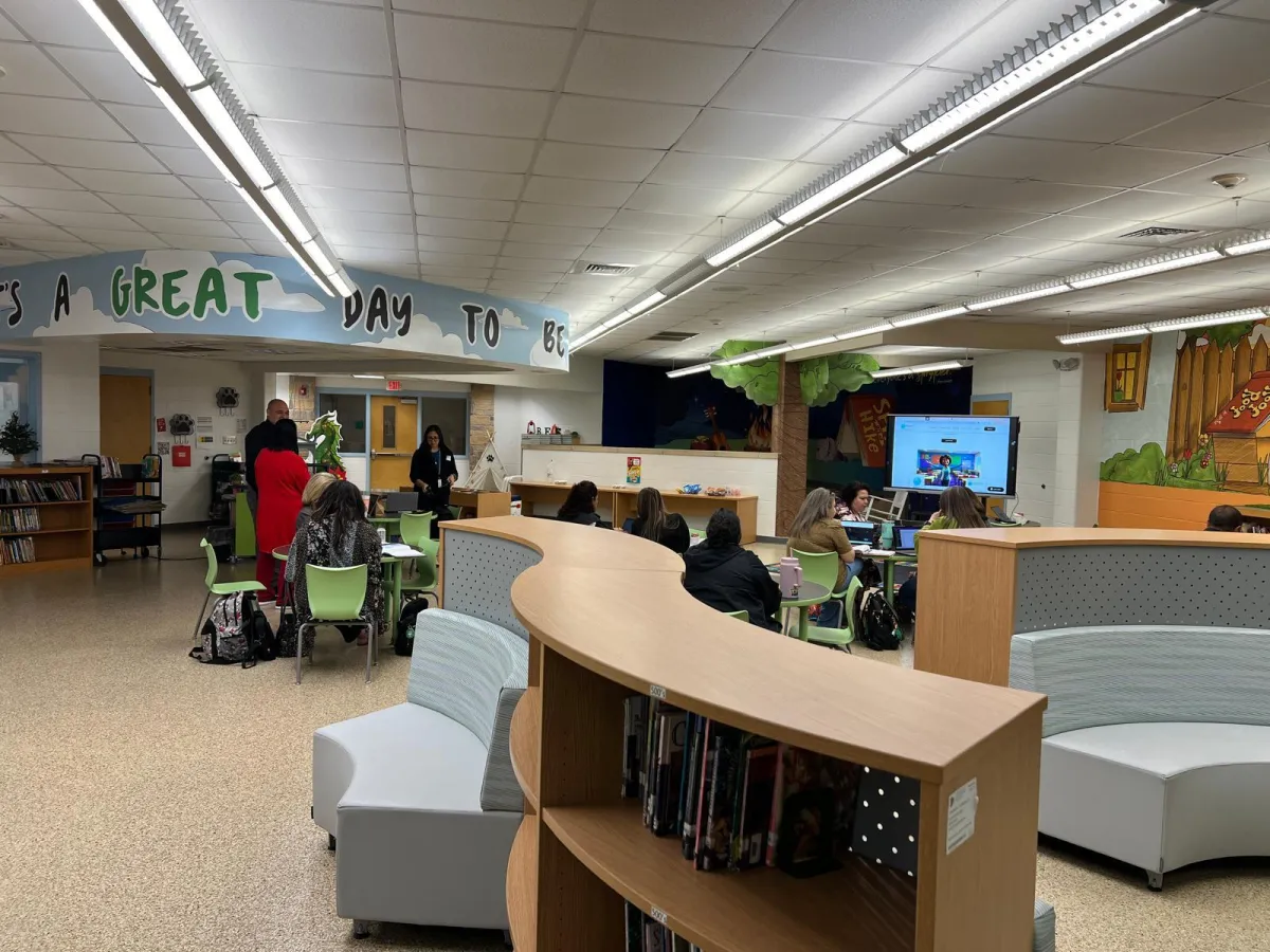 Educators in a school library training session, working on laptops in front of a presentation screen